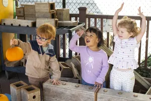 Three pre-schoolers cheer and clap on the playground of the Children's School